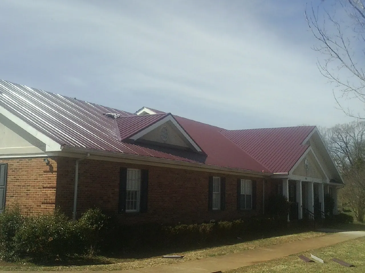 Red metal roof with gabled entries on a long brick building, from a Hail Damage Roof Repair job in Lincoln University