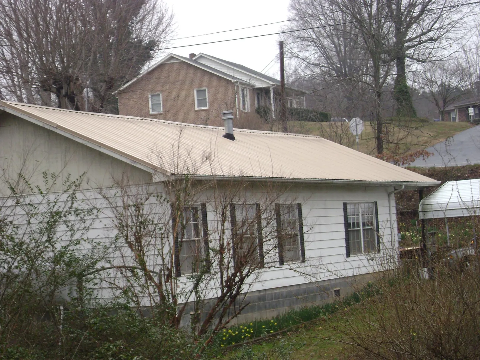 Tan metal roof on a white sided house set into a hillside — Commercial Roofing by Roofing Brothers in Lincoln University