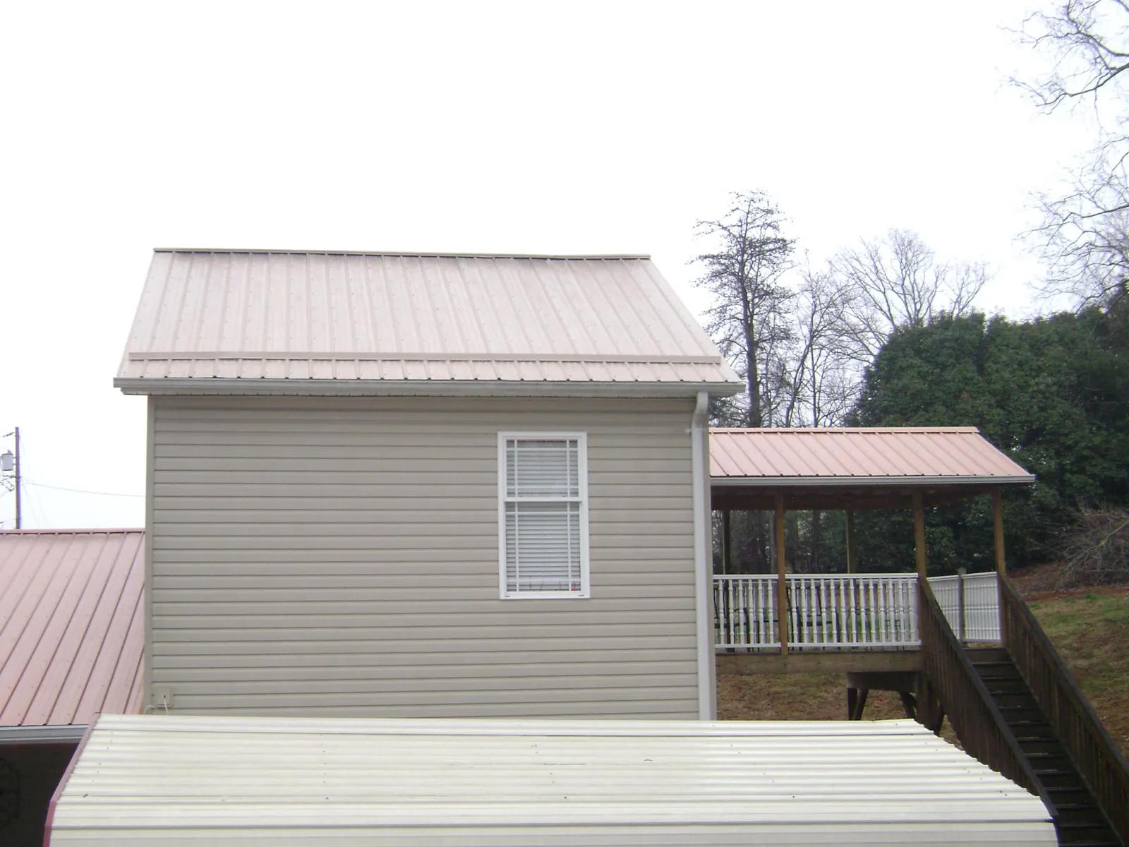 Tan metal roofs on a two story addition and attached porch, from a Roof Replacement job in Lincoln University